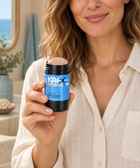 Woman holding KAFX Ocean Jetty deodorant in a warm coastal room